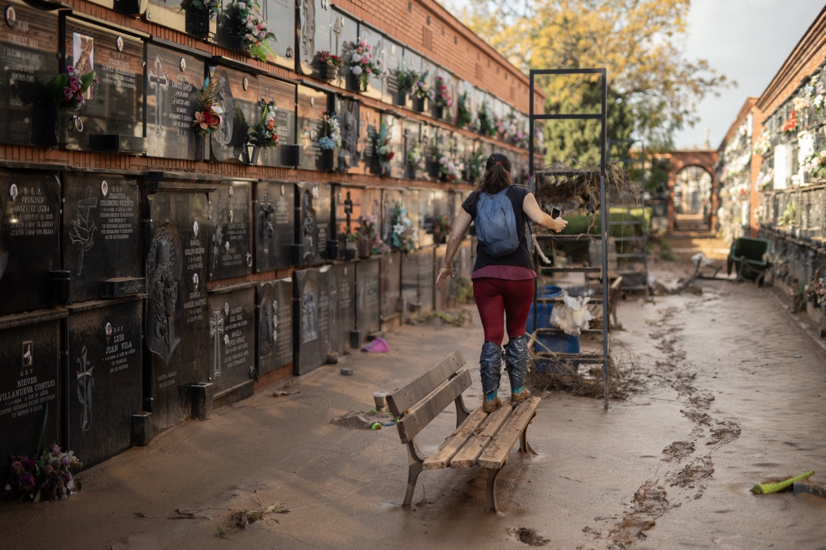 Una mujer subida a un banco para esquivar en el barro, en el cementerio de Alfafar.