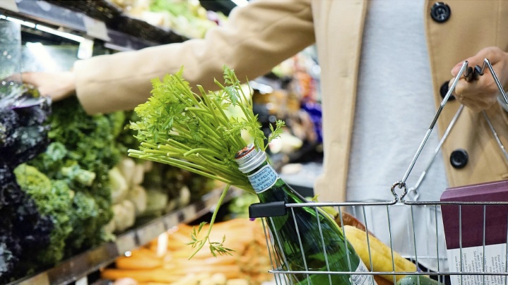 Persona comprando zanahorias frescas en supermercado, con cesta de compras y verduras al fondo.