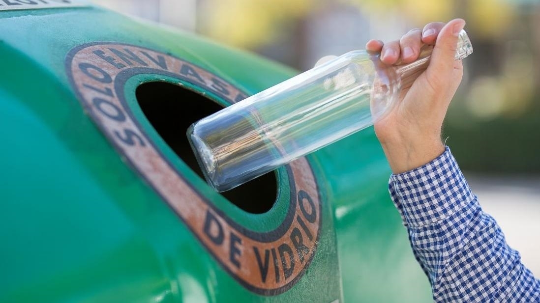 Una persona recicla vidrio en el contenedor verde.