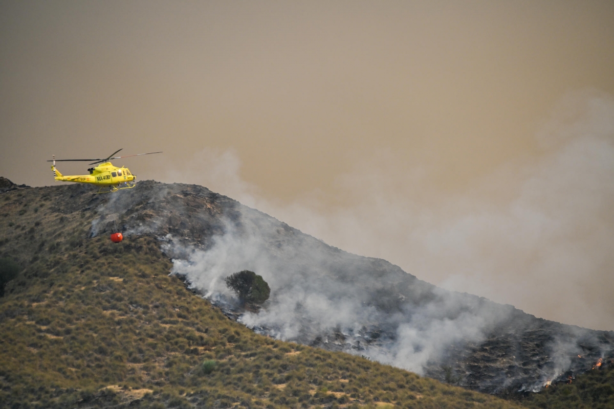 Un helicóptero del servicio de extinción de incendios arroja agua sobre uno de los focos del incendio.