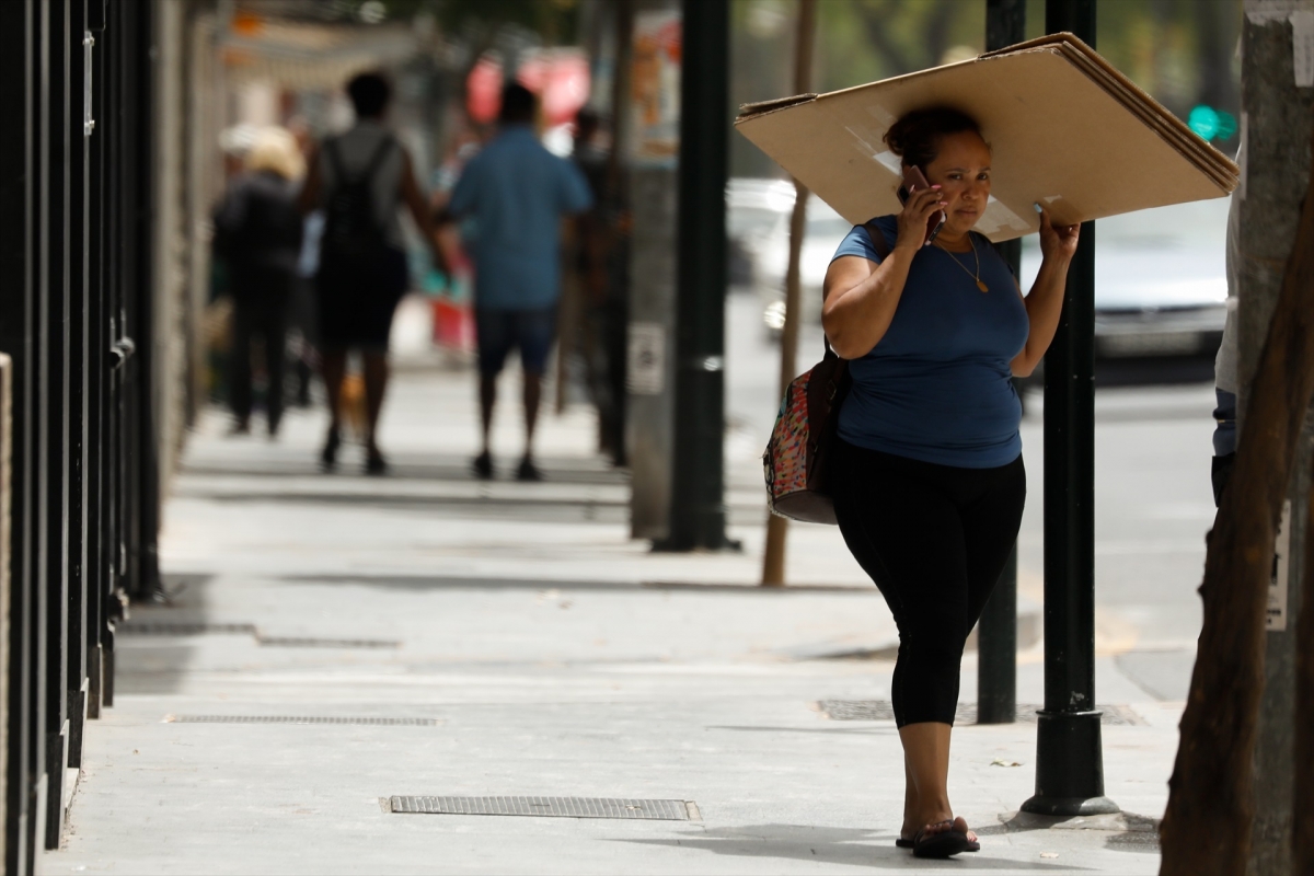 Una mujer se protege del sol con una caja de cartón.