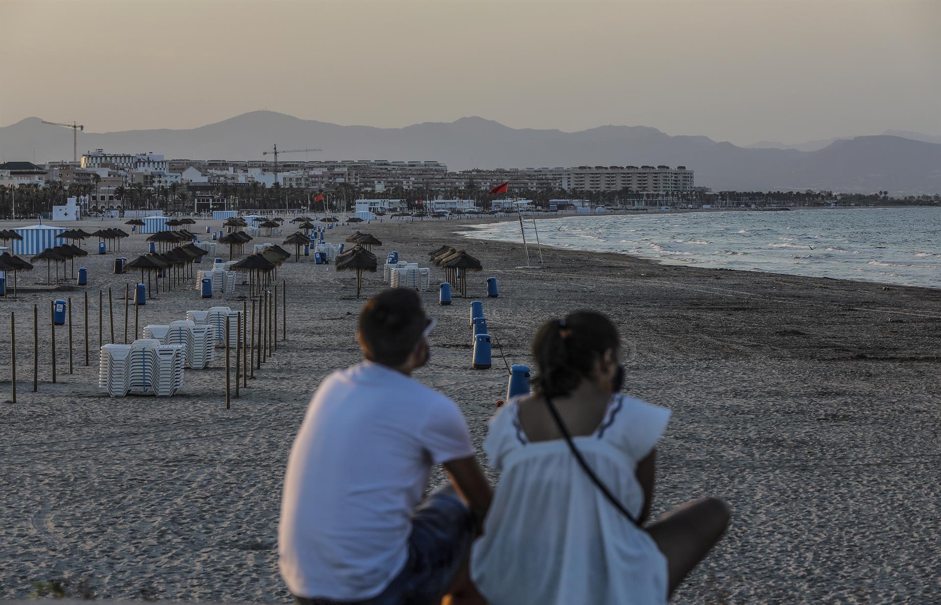 Dos jóvenes sentados contemplan la playa de la Malvarrosa. Foto: ROBER SOLSONA/EP - 