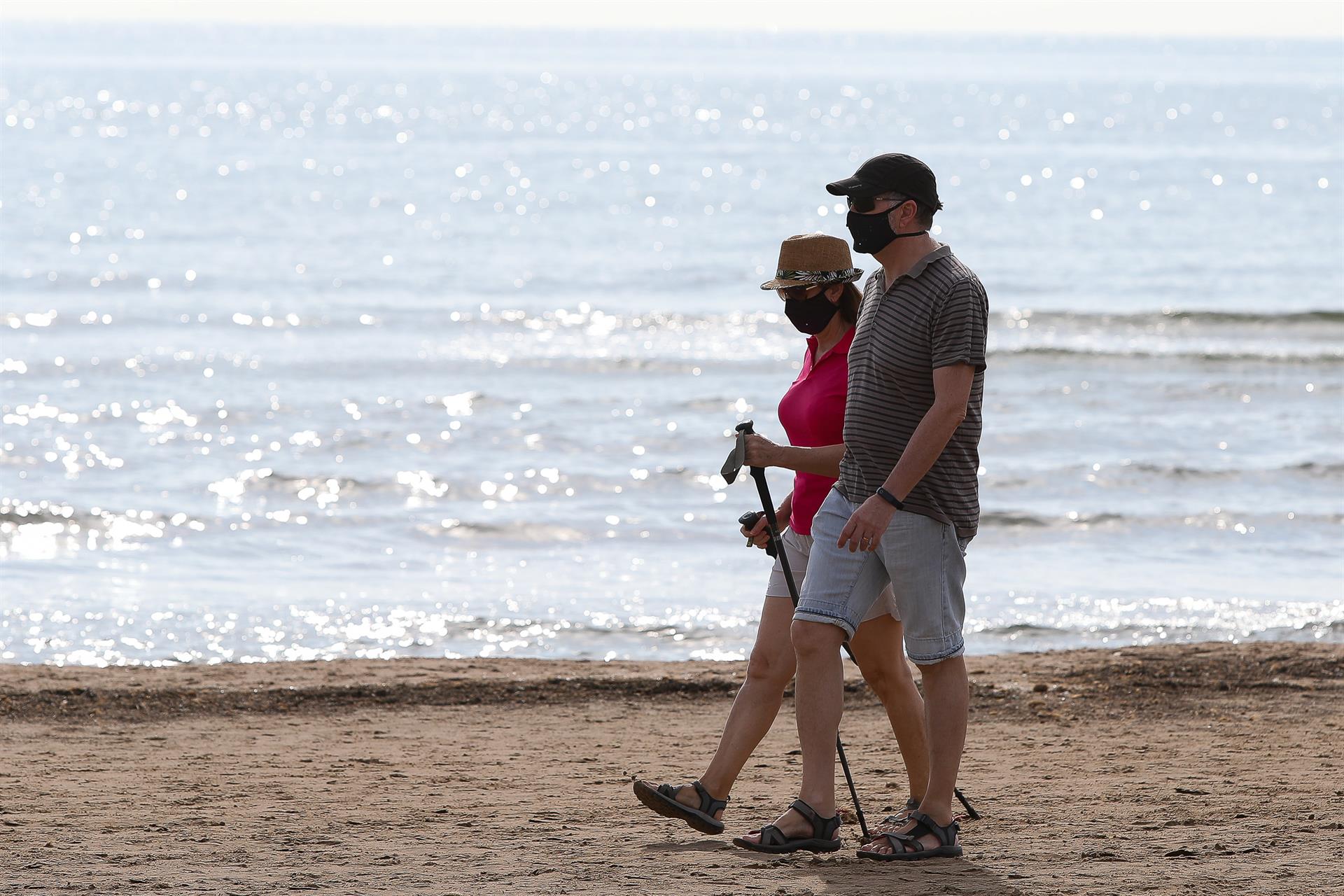 Dos personas protegidas con mascarilla pasean por la playa de la Malvarrosa . Foto: IVÁN TERRÓN (EP)  - 
