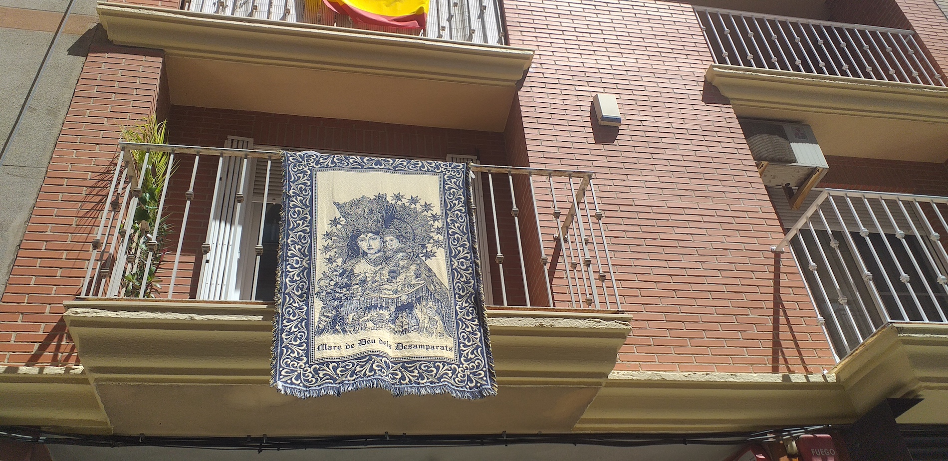 Un tapiz con la imagen de la Virgen de los Desamparados cuelga de un balcón.  - 