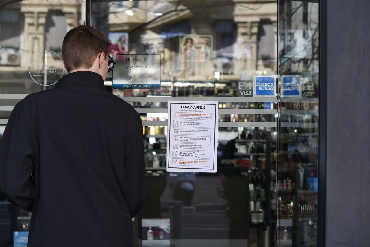 Un joven lee un cartel informativo con medidas especiales por el estado de alarma en un comercio de València. Foto: EDUARDO MANZANA - 