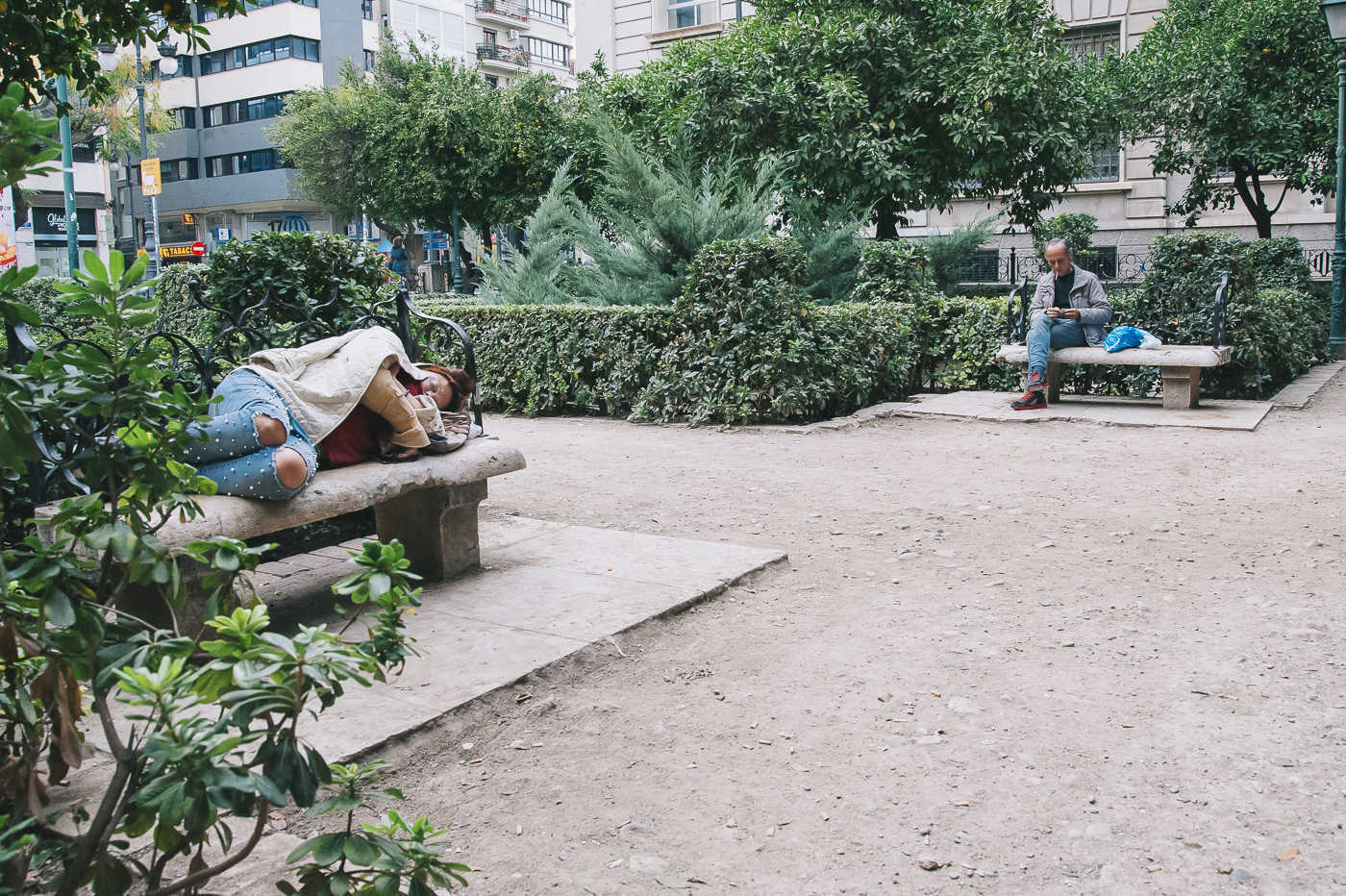 Una mendigo duerme mientras otro fuma un cigarro en un jardín de València. Foto: KIKE TABERNER - 